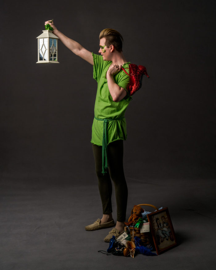 actor with red ruby slippers slung over his shoulder holding a lantern